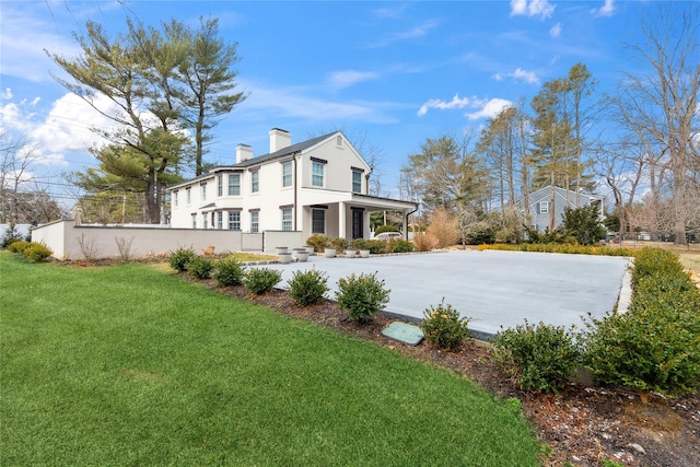 rear view of property featuring a yard, stucco siding, a chimney, and fence