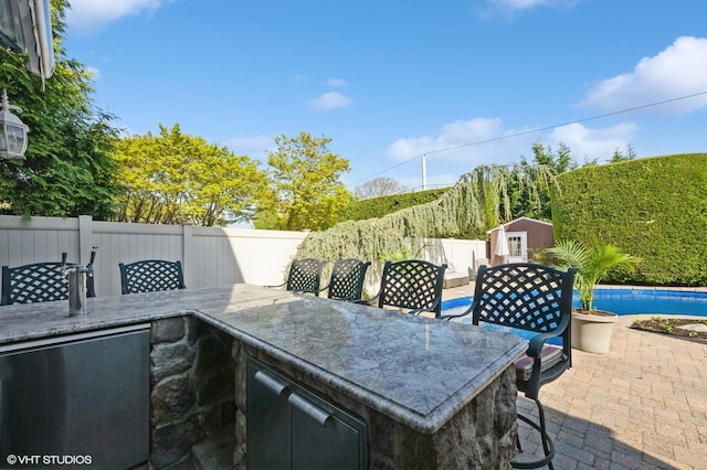 view of patio featuring a storage shed, an outbuilding, a fenced backyard, and outdoor dry bar