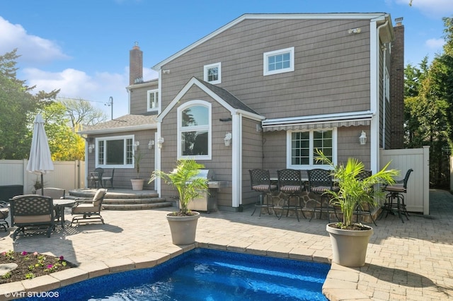 back of property featuring fence, outdoor dry bar, a chimney, a fenced in pool, and a patio area