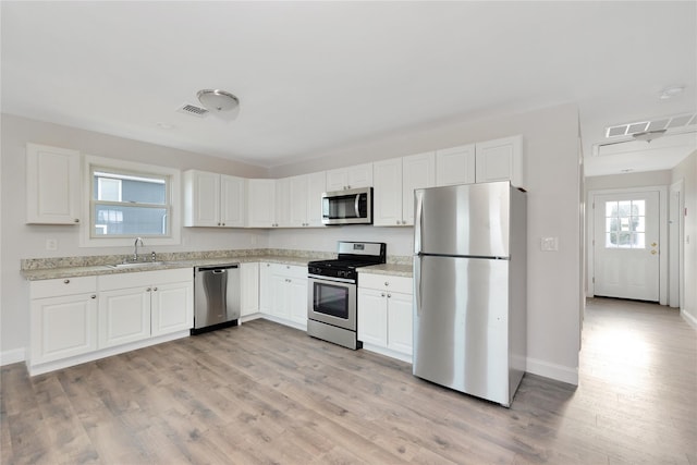 kitchen with a sink, stainless steel appliances, light wood-style flooring, and white cabinets