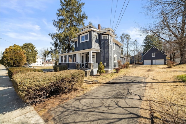 view of front facade with a detached garage, an outbuilding, a chimney, and driveway