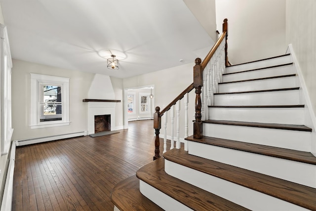 stairway with baseboard heating, a baseboard heating unit, a large fireplace, and hardwood / wood-style floors