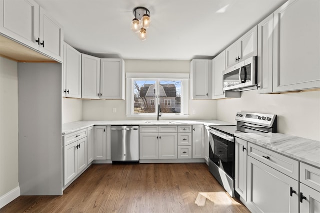 kitchen featuring a sink, dark wood-style floors, appliances with stainless steel finishes, white cabinets, and light stone countertops