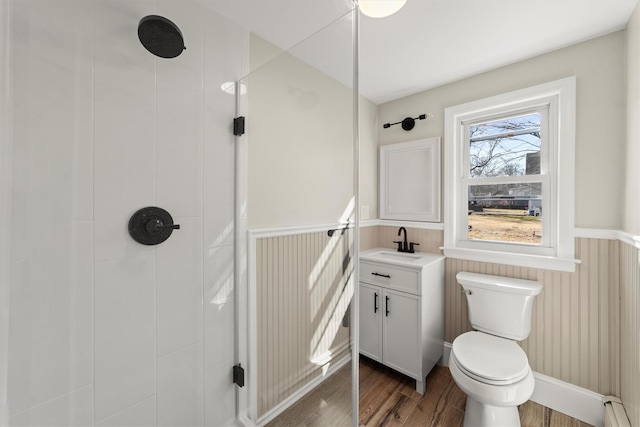 bathroom with wood finished floors, a baseboard radiator, a tile shower, wainscoting, and toilet