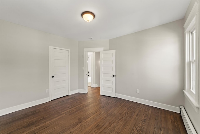 unfurnished bedroom featuring a baseboard heating unit, baseboards, and dark wood-type flooring