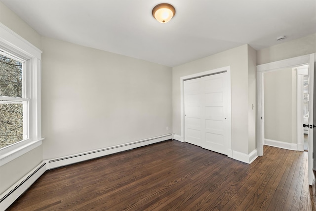 unfurnished bedroom featuring baseboards, multiple windows, dark wood-type flooring, and baseboard heating