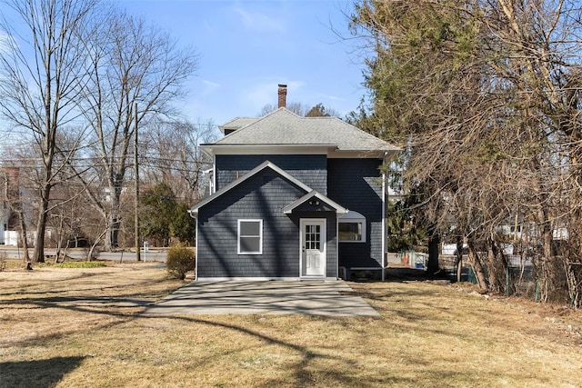 view of front of property with a front lawn, roof with shingles, and a chimney