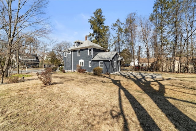 back of house with a yard, driveway, a chimney, and a shingled roof