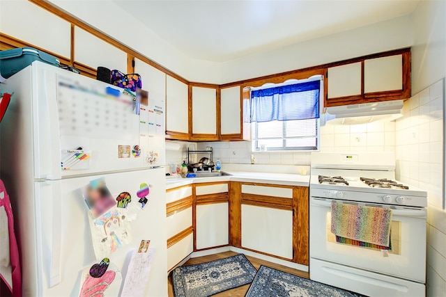 kitchen with backsplash, under cabinet range hood, light countertops, white appliances, and a sink