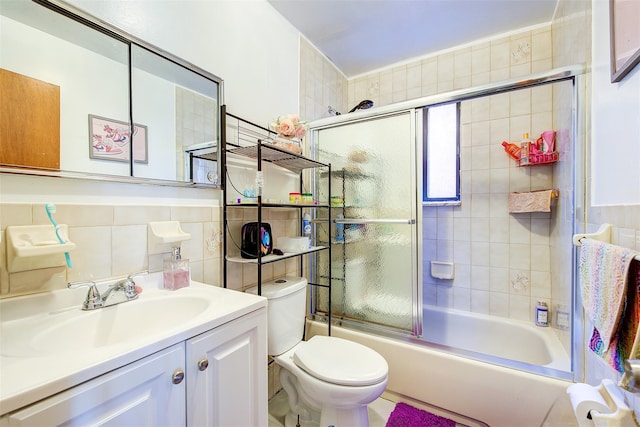 bathroom featuring combined bath / shower with glass door, toilet, tile walls, and vanity