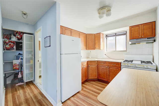 kitchen with light wood-style flooring, under cabinet range hood, a sink, white appliances, and light countertops