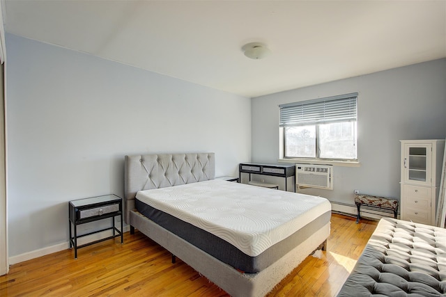 bedroom with a baseboard radiator, baseboards, an AC wall unit, and light wood finished floors