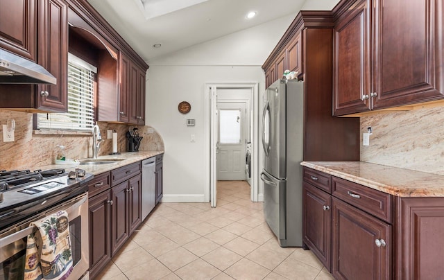 kitchen with a sink, light stone counters, appliances with stainless steel finishes, light tile patterned flooring, and vaulted ceiling