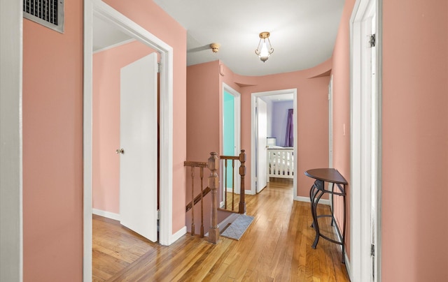 hallway with visible vents, an upstairs landing, baseboards, and light wood-style flooring