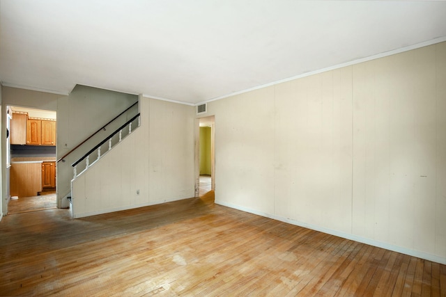 unfurnished living room featuring light wood finished floors, visible vents, stairs, and ornamental molding