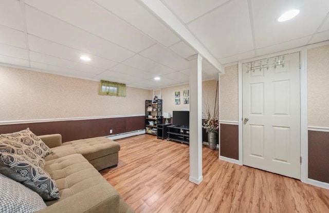 living room featuring a drop ceiling, a wainscoted wall, light wood-style floors, and a baseboard radiator