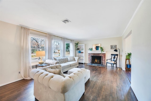 living room with visible vents, a brick fireplace, baseboards, ornamental molding, and dark wood-style floors