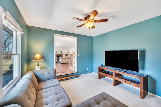 living area with a ceiling fan, stairway, a fireplace, carpet flooring, and baseboards