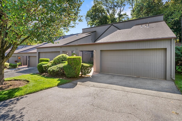 mid-century modern home with driveway, a shingled roof, and a garage