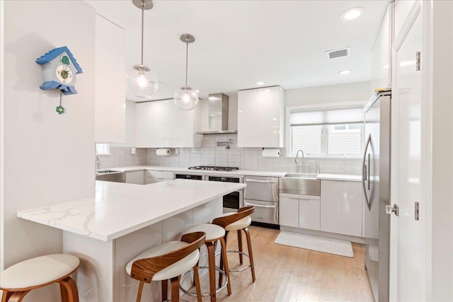 kitchen with wall chimney range hood, visible vents, white cabinets, and a sink