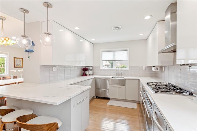 kitchen featuring visible vents, stainless steel gas stovetop, a peninsula, white cabinets, and wall chimney range hood