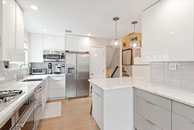 kitchen featuring a peninsula, stainless steel appliances, white cabinetry, modern cabinets, and a sink