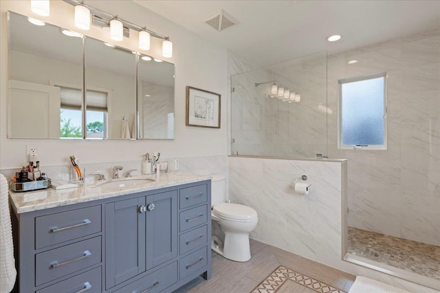 bathroom featuring visible vents, toilet, a marble finish shower, tile walls, and vanity