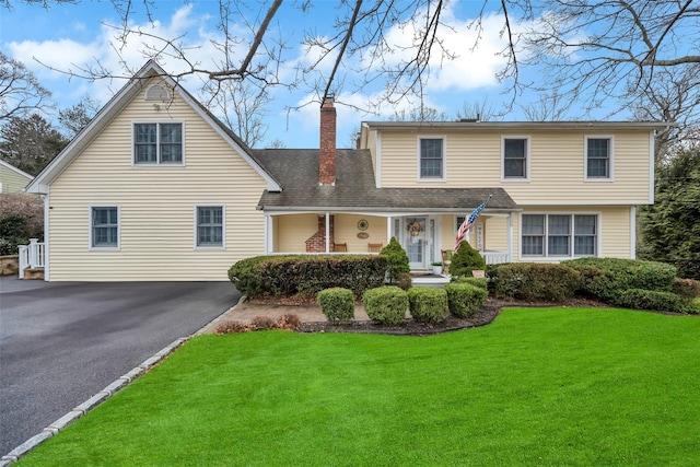 view of front of home with aphalt driveway, a front yard, roof with shingles, and a chimney