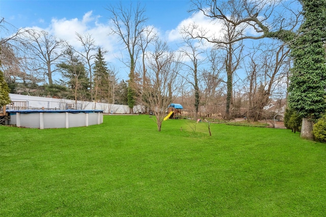 view of yard with a covered pool, a playground, and fence