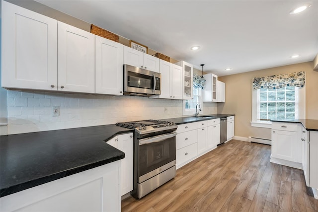 kitchen with light wood finished floors, dark countertops, backsplash, appliances with stainless steel finishes, and white cabinetry