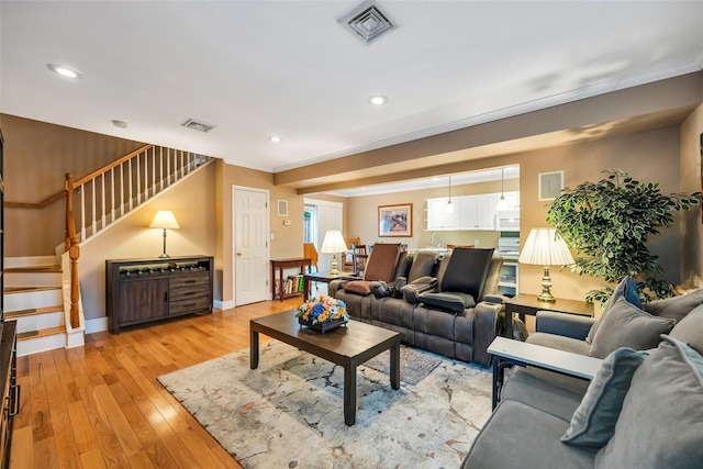 living area featuring crown molding, stairway, visible vents, and light wood finished floors