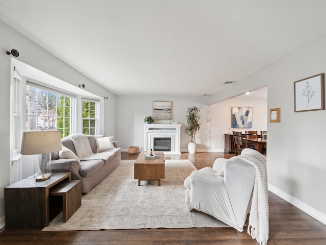 living area with a glass covered fireplace, visible vents, baseboards, and wood finished floors