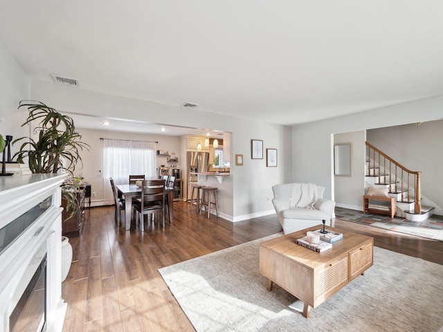 living area with wood finished floors, visible vents, baseboards, a fireplace, and stairs