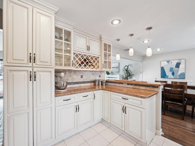 kitchen with pendant lighting, light tile patterned floors, decorative backsplash, light stone counters, and a peninsula