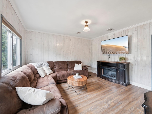 living area with visible vents, wood finished floors, a glass covered fireplace, and ornamental molding