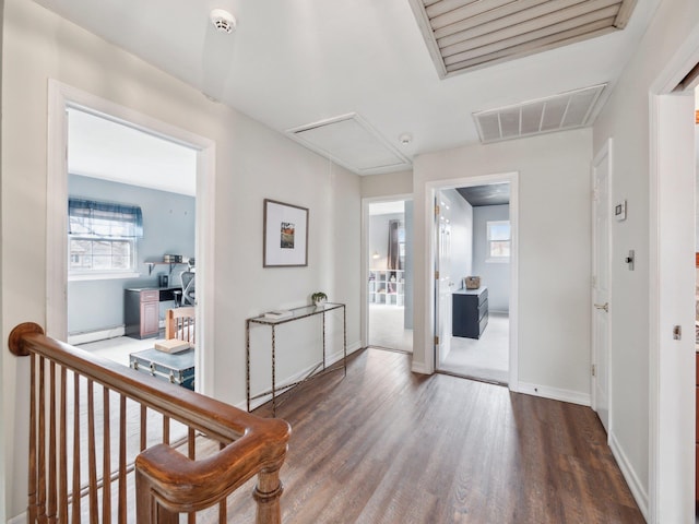 hallway featuring visible vents, a baseboard heating unit, wood finished floors, baseboards, and attic access