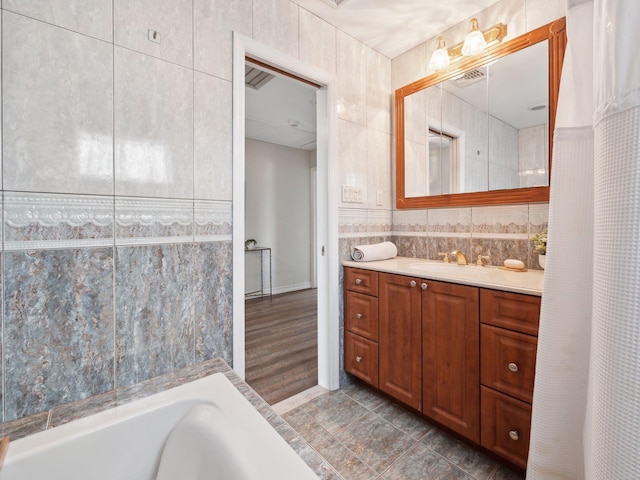 bathroom with vanity, tile walls, a tub to relax in, and visible vents