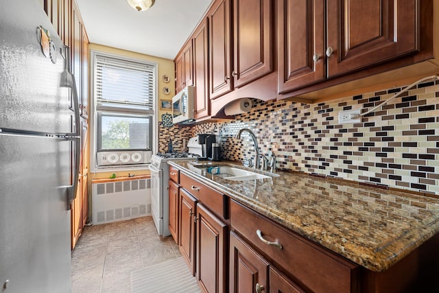 kitchen featuring dark stone counters, radiator heating unit, decorative backsplash, white appliances, and a sink