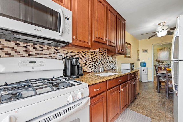 kitchen featuring tasteful backsplash, light stone counters, white appliances, a ceiling fan, and a sink