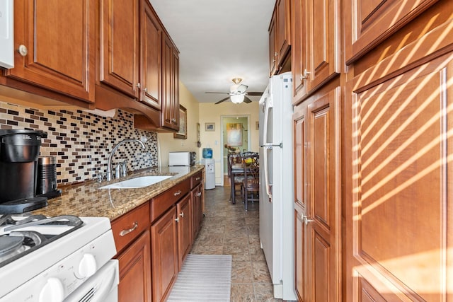 kitchen featuring backsplash, light stone countertops, brown cabinetry, white appliances, and a sink