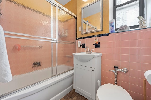 bathroom with combined bath / shower with glass door, toilet, tile walls, and a sink