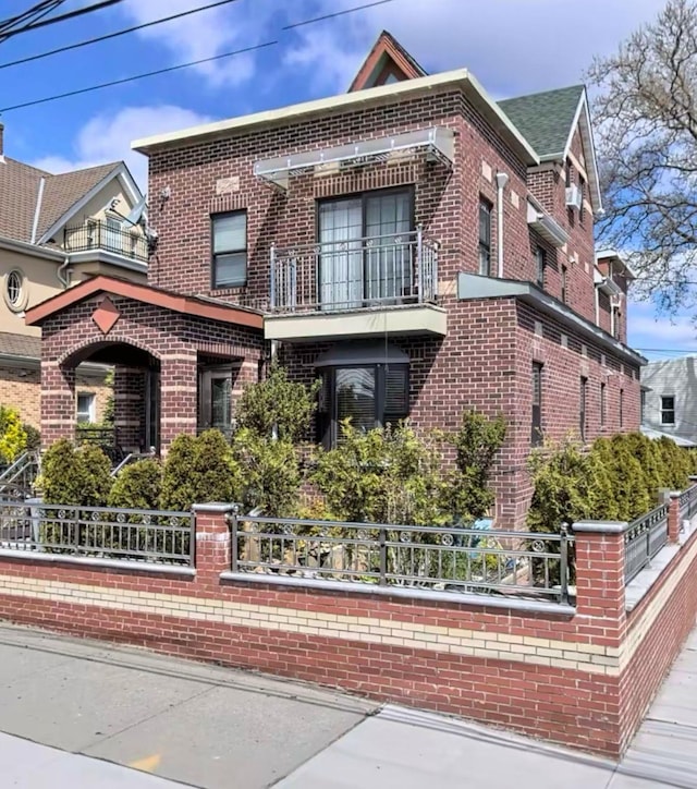 view of front of home with a balcony, brick siding, and a fenced front yard