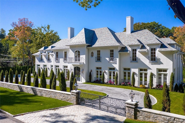 view of front facade featuring driveway, a front lawn, a balcony, and a chimney