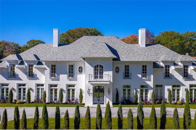 view of front of property featuring a high end roof, french doors, a chimney, and a balcony