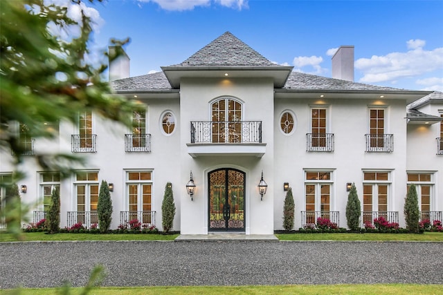 french country inspired facade featuring french doors, a balcony, a chimney, and stucco siding