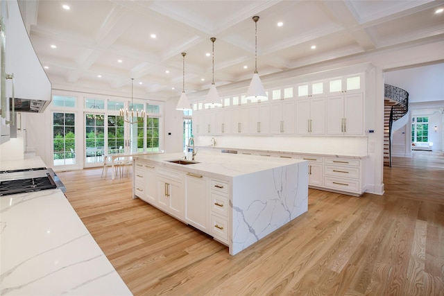 kitchen featuring light wood finished floors, island exhaust hood, white cabinets, coffered ceiling, and a sink