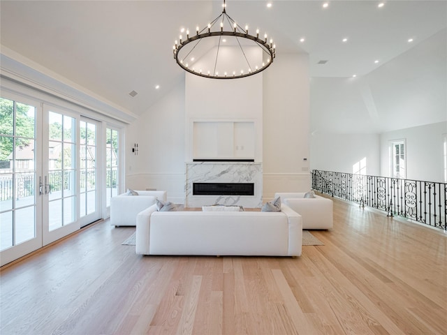 living area featuring french doors, high vaulted ceiling, light wood-type flooring, and a premium fireplace