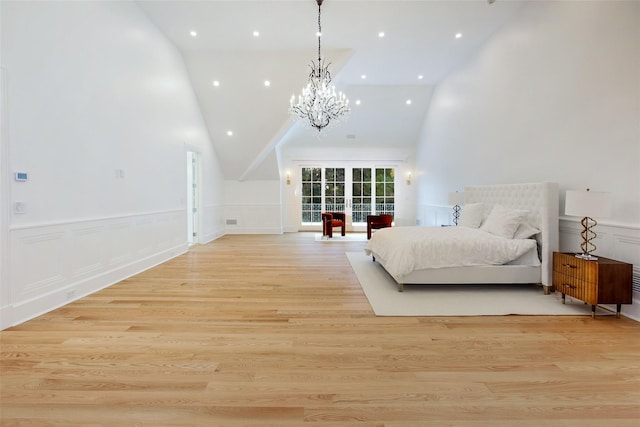 bedroom featuring light wood-type flooring, a wainscoted wall, a notable chandelier, a decorative wall, and a towering ceiling