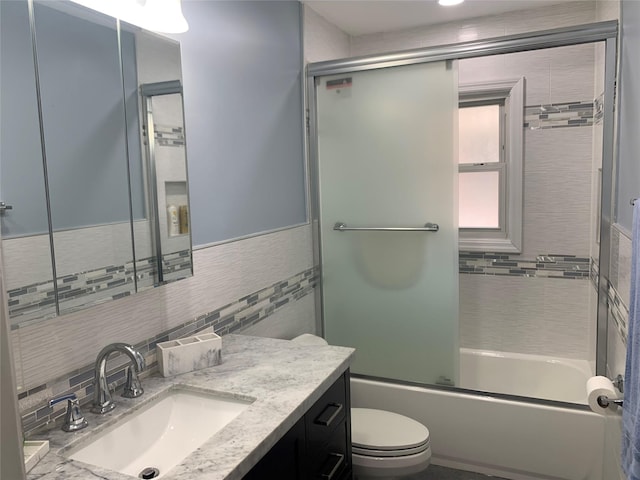 bathroom featuring vanity, tile walls, toilet, and bath / shower combo with glass door