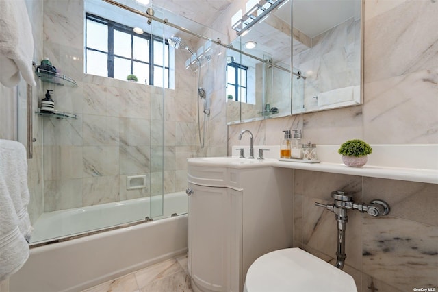 bathroom featuring toilet, marble finish floor, combined bath / shower with glass door, tile walls, and vanity